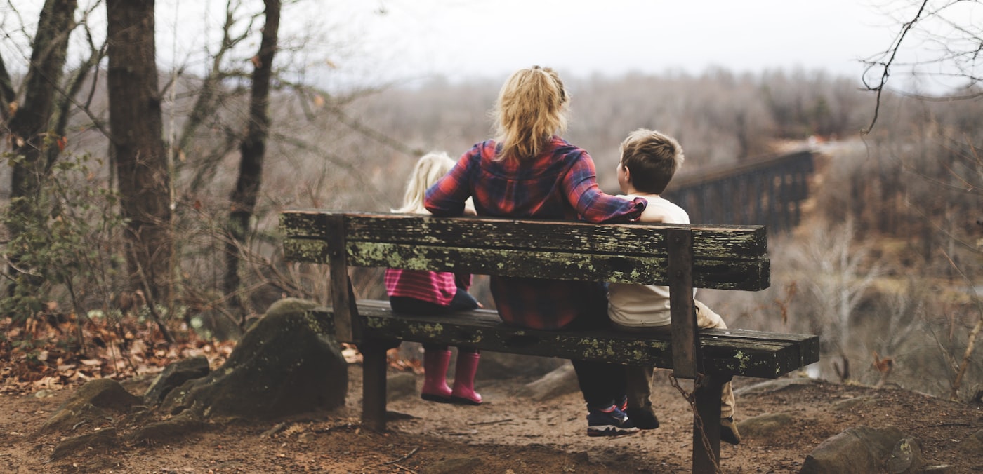 Una madre seduta su una panchina in mezzo alla natura con due bambini